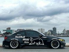 a black sports car parked in front of a body of water with a city skyline behind it