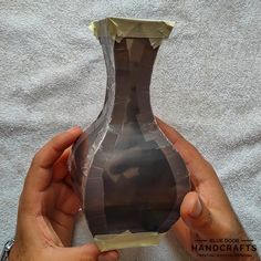 a person holding a brown vase in their hands on a white sheeted cloth background