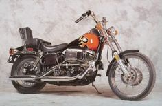 an orange and black motorcycle is parked in front of a gray wall with no one on it