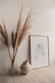 there is a vase with some dry grass in it next to a painting on the wall