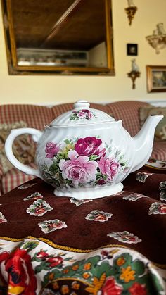 a tea pot with flowers painted on it sitting on a bed in front of a mirror