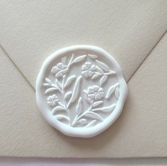 a close up of a white wax seal on an envelope with flowers and leaves in it