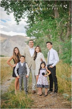 a family posing for a photo in front of some trees and grass with mountains in the background