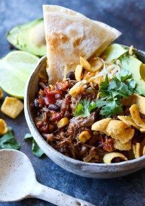 a bowl filled with taco salad next to tortilla chips and avocado