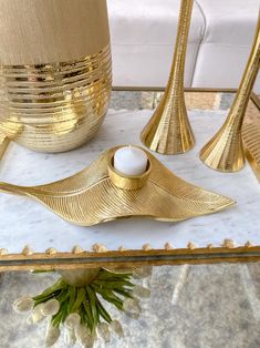 three gold vases and two candles on a marble table