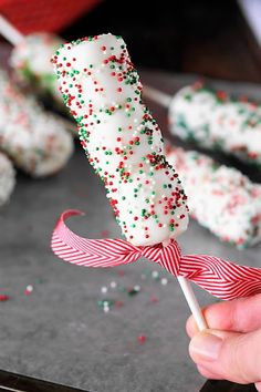 a hand holding a candy cane with sprinkles on it and red and white striped ribbon