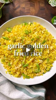 a white bowl filled with yellow rice on top of a wooden table next to green leaves