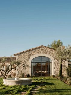 a stone house with an olive tree in the foreground and grass on the ground