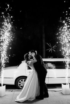 a bride and groom kissing in front of their wedding car with sparklers on the ground