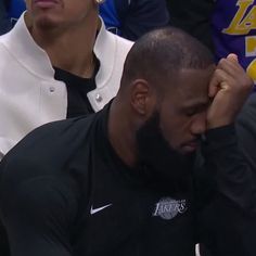 the lakers player is holding his head while sitting in front of other people at a basketball game