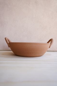 a wooden bowl with handles on a white tableclothed floor next to a beige wall