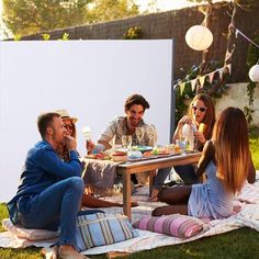 a group of people sitting at a picnic table eating food and drinking wine while talking to each other