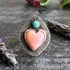 This sweet pink Queen Conch heart is set on a hand stamped sterling silver backplate and is topped with a round Kingman turquoise cabochon. Patina was added for depth and interest. It sits on a sterling silver adjustable band. Right now, the band is sized at around 4. Let me know what size you want and I'll adjust it up to that size (up to around a size 12). Please note that this is handmade item using natural materials and, as such, may contain minor imperfections. That's the beauty of not buying mass-produced jewelry, though -- you get a one-of-a-kind piece! Listing is for one ring. Your new jewel will be packaged in a muslin gift pouch and inside its own box. I include a silver polishing cloth with each sterling silver piece of jewelry so you can keep it as shiny and beautiful as the da Bohemian Stamped Turquoise Ring Gift, Handmade Pink Heart-shaped Ring, Stamped Turquoise Rings For Gifts, Gift Turquoise Sterling Silver Ring, Sterling Silver Stamped Turquoise Ring Gift, Handmade Bohemian Heart-shaped Rings, Bohemian Handmade Heart Ring Gift, Handmade Bohemian Heart Ring Gift, Southwestern Style Pink Jewelry Gift