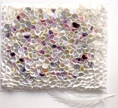 a piece of art made out of buttons and paper with a feather on the side