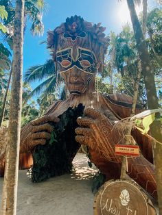 there is a large wooden statue that looks like a human face in the sand with palm trees around it