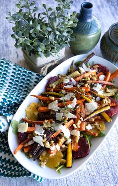 a white platter filled with carrots and other veggies next to a potted plant