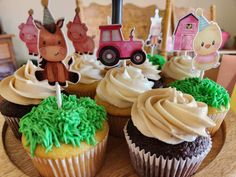 cupcakes decorated with farm animals and green frosting on a wooden table top