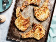 chicken cut in half on a baking sheet with fork and knife next to the plate