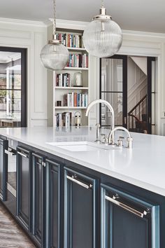 a large kitchen with white counter tops and blue cabinets, along with two hanging lights