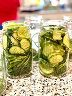 three jars filled with cucumbers sitting on top of a counter