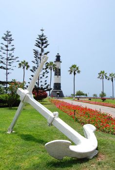 a large white anchor sitting on top of a lush green field next to a light house