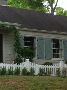 a white picket fence in front of a gray house with blue shutters on the windows