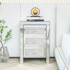 a white bed sitting next to a silver night stand with two drawers on top of it