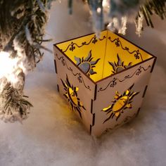 an origami box sitting in the snow next to a christmas tree with lights on it