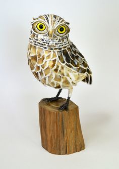 an owl figurine sitting on top of a piece of wood with yellow eyes