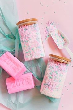 three jars filled with pink and blue sprinkles next to two spoons