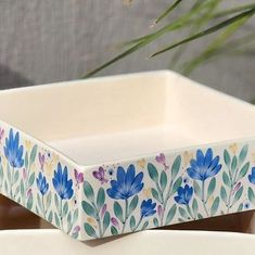 two white dishes with blue flowers painted on them and one has a plant in the background