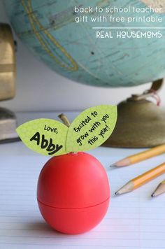 a red apple sitting on top of a desk next to pencils