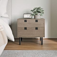 a nightstand with a clock and plant on it next to a bed in a bedroom