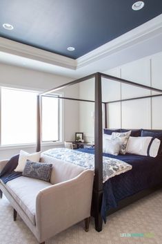 a bedroom with a four poster bed and white walls, carpeted flooring and blue ceiling