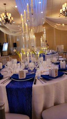 a banquet table with blue and white linens, silver place settings and centerpieces