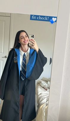 a woman taking a selfie in front of a mirror wearing a graduation robe and holding a cell phone