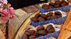 some chocolates are sitting in blue boxes on a wooden table next to pink flowers