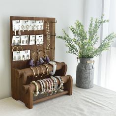 a wooden jewelry rack with bracelets and rings on it next to a vase filled with flowers