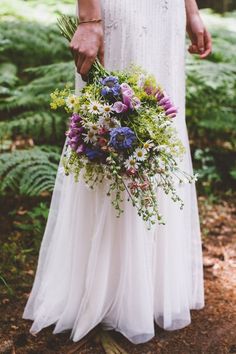 a woman in a white dress holding a bouquet of wildflowers and greenery