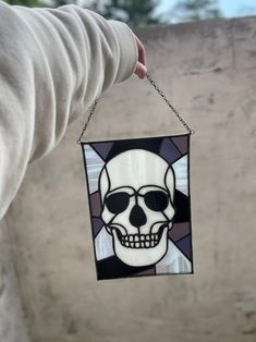 a hand holding a stained glass skull hanging from a chain on a wall with trees in the background