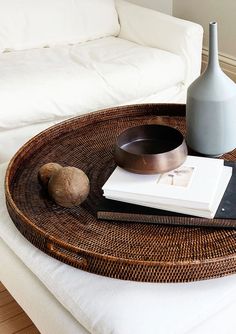 a wicker tray with a book, bowl and vase sitting on top of it