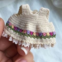 a crocheted baby dress is being held by someone's hand with white nails