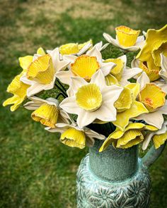 a green vase filled with yellow flowers on top of a grass covered field next to a lawn