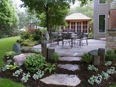 an outdoor patio and dining area with stone steps leading up to the back door, surrounded by greenery