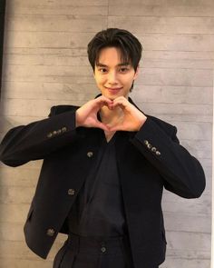 a young man making a heart with his hands while standing in front of a wall