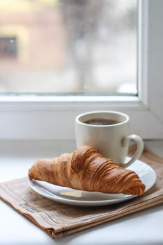 a croissant on a plate next to a cup of coffee