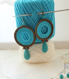 a pair of earrings sitting on top of a ball of yarn next to a crochet doily