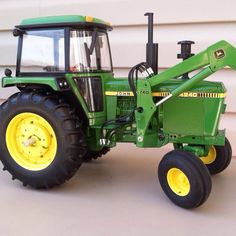 a green toy tractor sitting on top of a white floor next to a building with yellow wheels