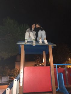 two people sitting on top of a blue and red structure in front of a dark sky