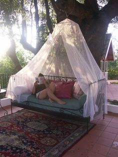 a woman sitting on top of a bed next to a tree with a canopy over it